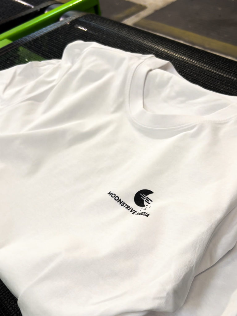 Für Moonstrive Media mit Siebdruck veredeltes weißes T-Shirt.